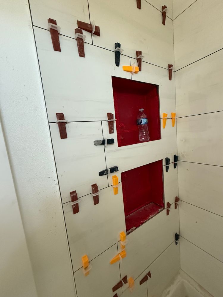 White tiled wall with two red recessed panels and orange-black tile spacers in progress