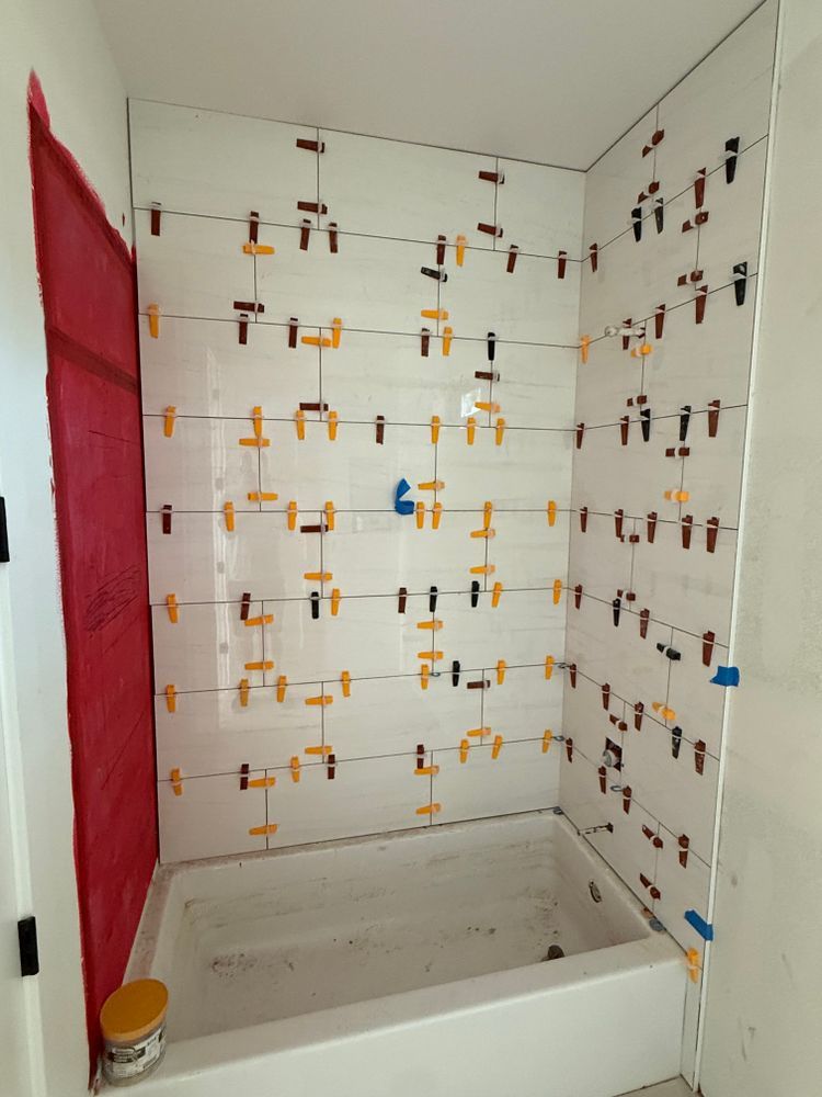 Tiled shower alcove under renovation with tile leveling clips and a red protective tarp on the left.