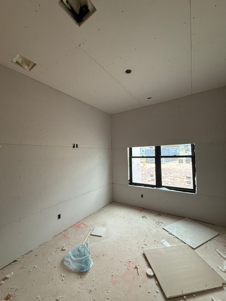 Bare unfinished room with debris on the floor and a window letting in daylight.
