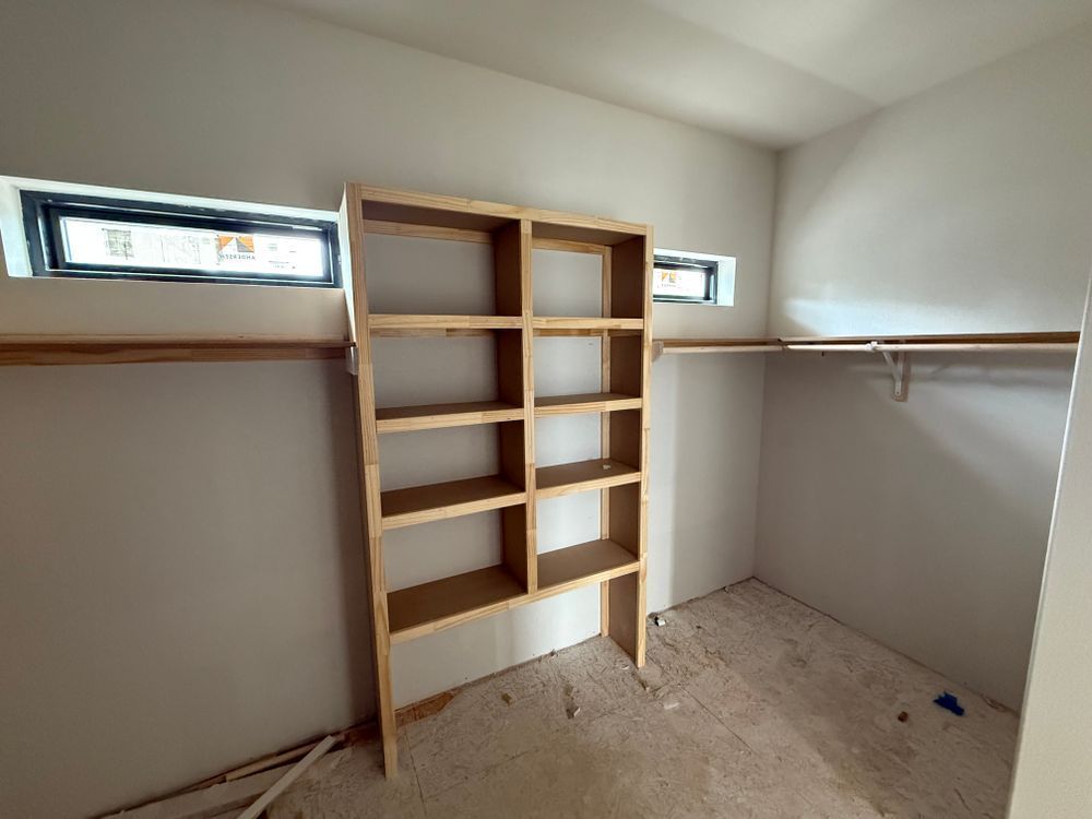 Small walk-in closet with built-in shelves, hanging rods, and two narrow windows.