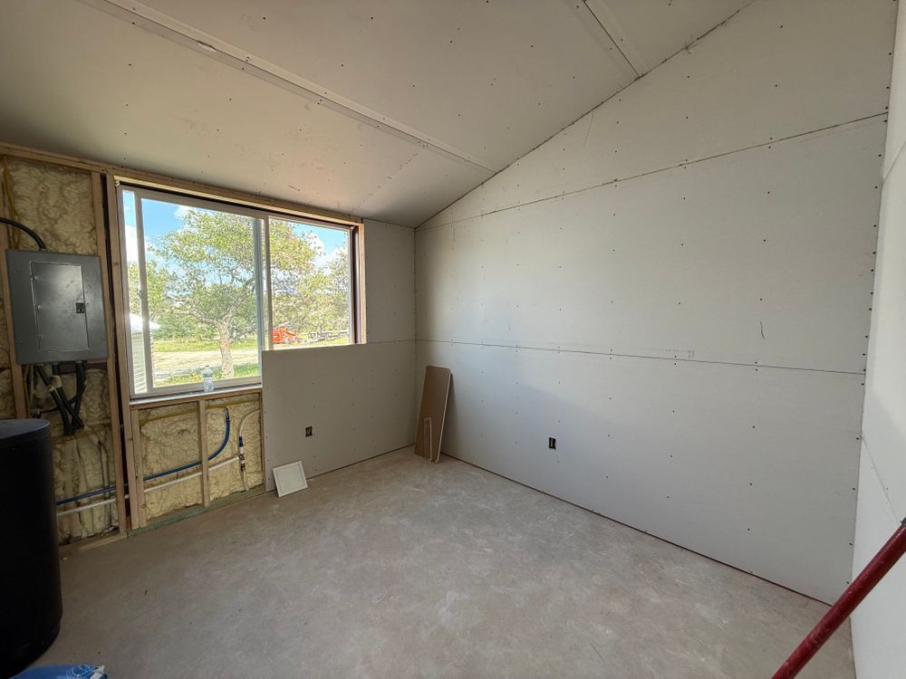 Empty unfinished room with bare walls, carpet, and a window overlooking trees.