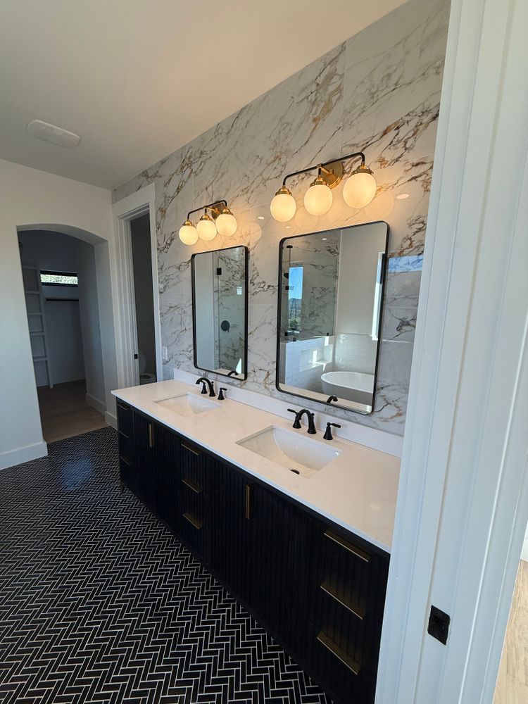 Modern bathroom vanity with two mirrors, globe lights, white marble wall, and patterned dark floor.