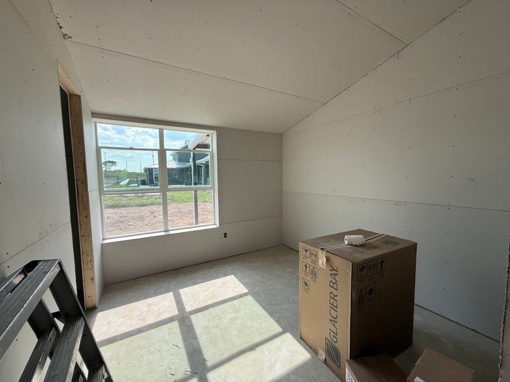 Empty unfinished room with white walls, a large window, and a cardboard box on the floor