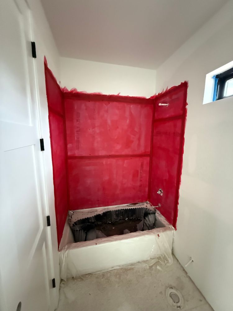 Small bathroom alcove with red waterproofed walls and a recessed floor opening under construction.