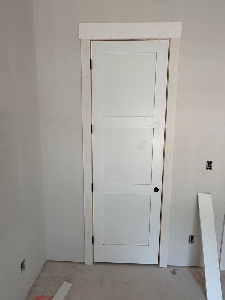 White interior door in a bare room with unfinished walls and a small floor opening near the baseboard.