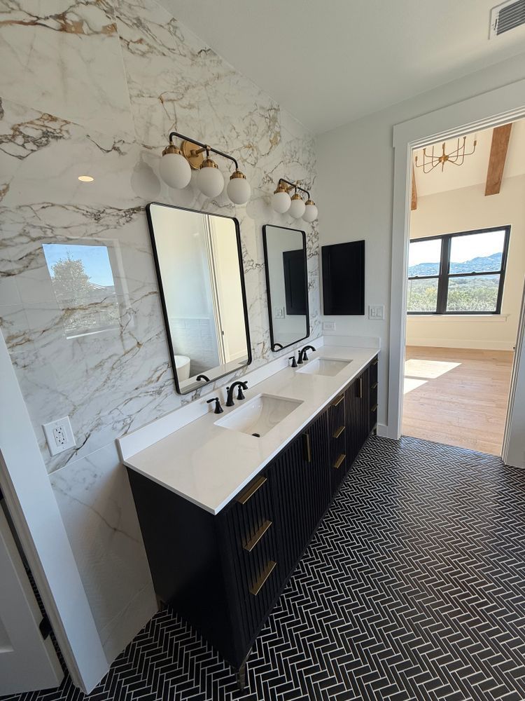 Modern bathroom vanity with white marble walls, black cabinets, and patterned floor leading to a bright adjoining room