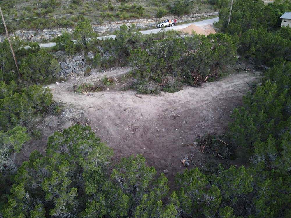 Overgrown dirt clearing beside a road, surrounded by dense green vegetation.