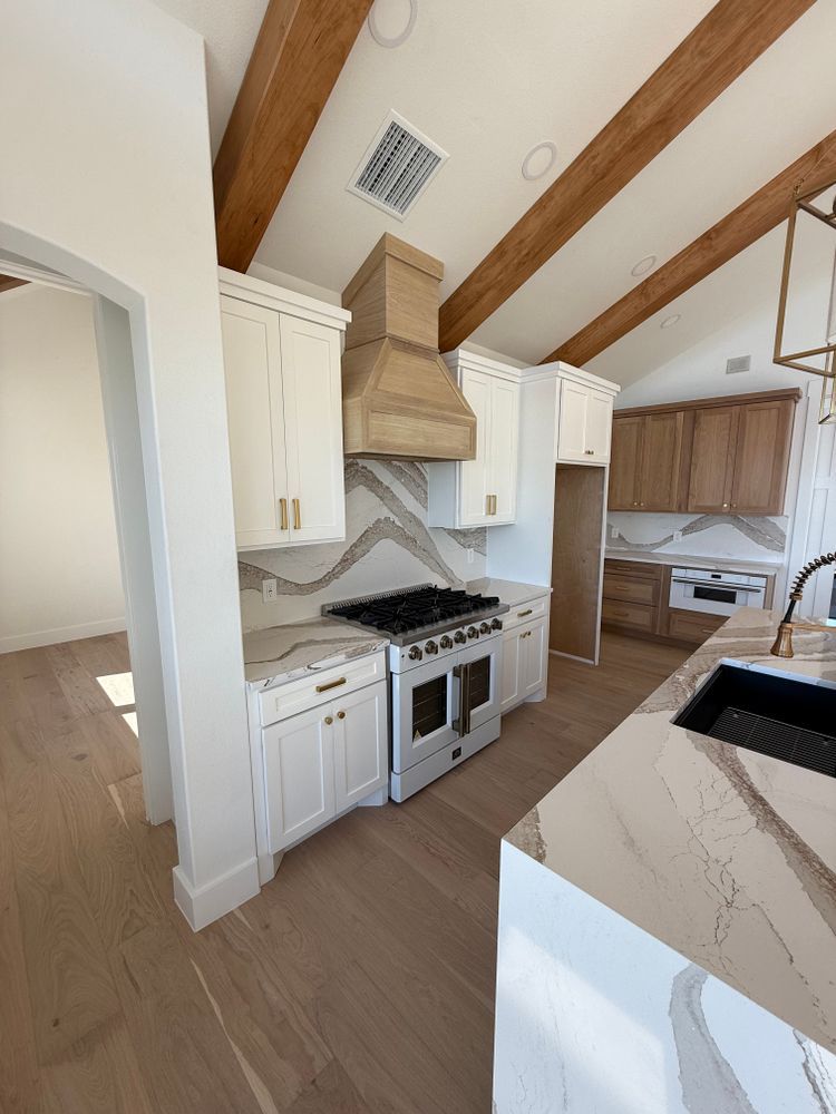 Modern kitchen with vaulted wood ceiling, white cabinets, stainless range, and marble island countertop