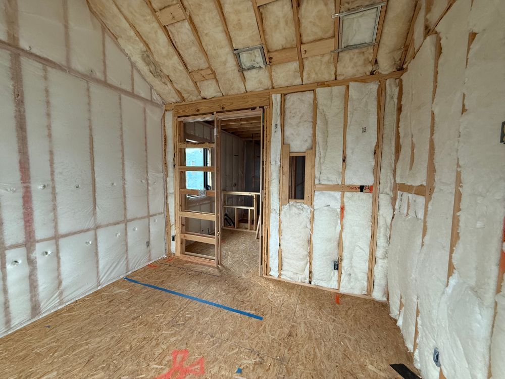 Unfinished room with white insulated walls, exposed wood framing, and plywood floor opening to a doorway.