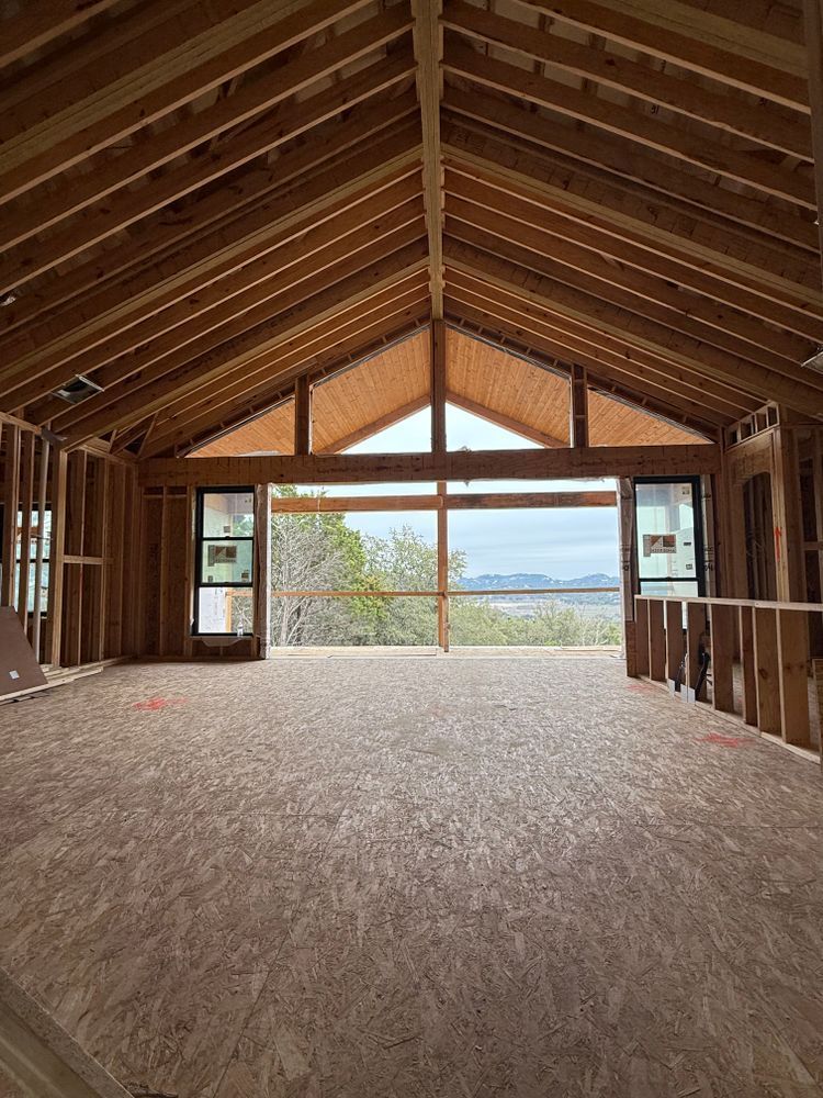 Empty wooden loft room with exposed rafters, carpeted floor, and large windows overlooking water