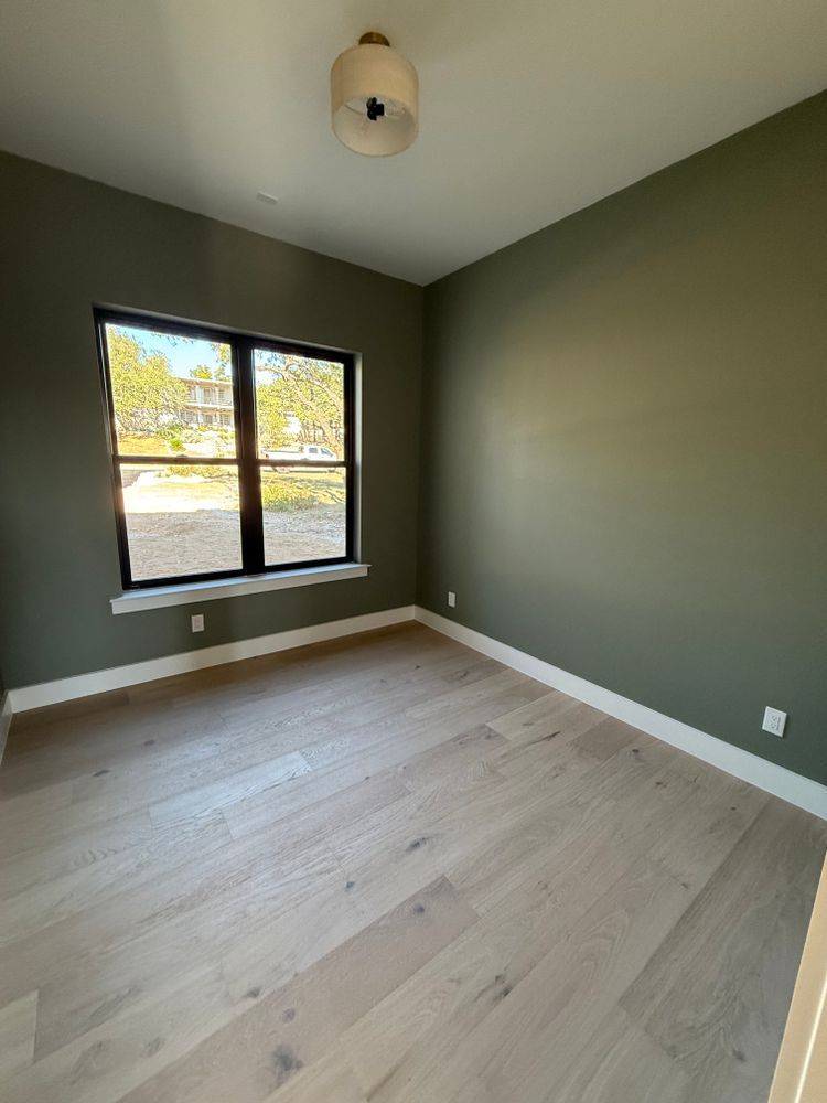 Empty bedroom with olive-green walls, light wood floors, and a window letting in daylight