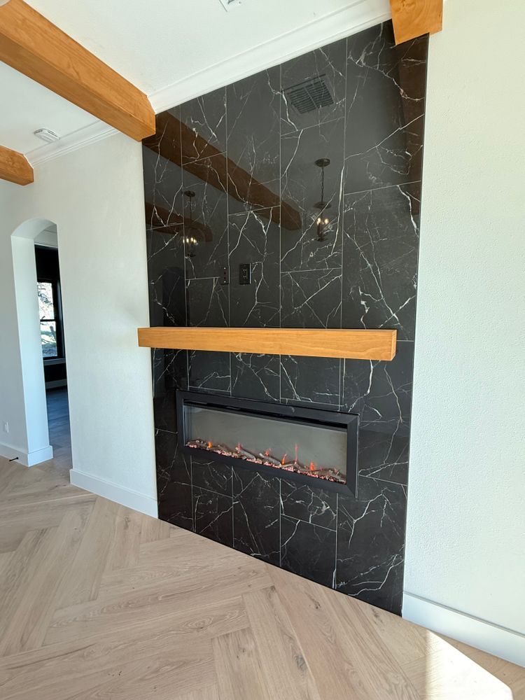 Modern living room corner with black marble fireplace, wooden mantel, and herringbone wood floor