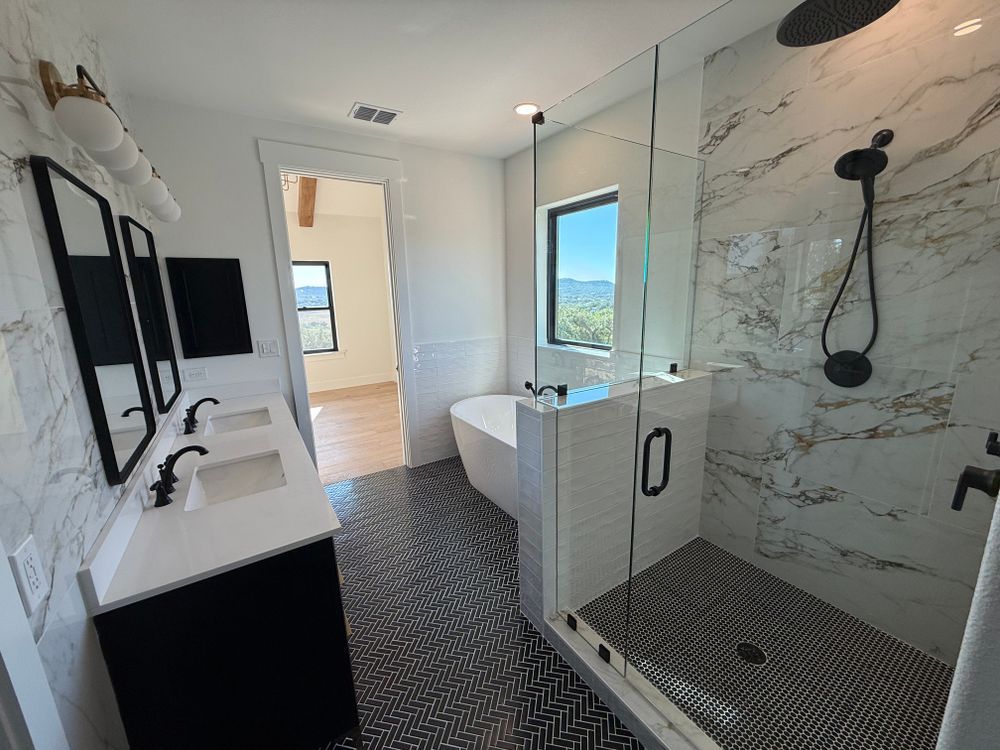 Modern bathroom with black-and-white vanity, glass shower, and window view of greenery