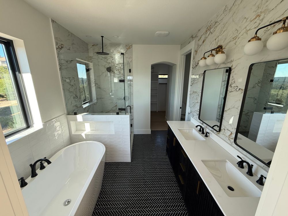 Bright modern bathroom with soaking tub, double vanity, shower, and dark patterned tile floor.