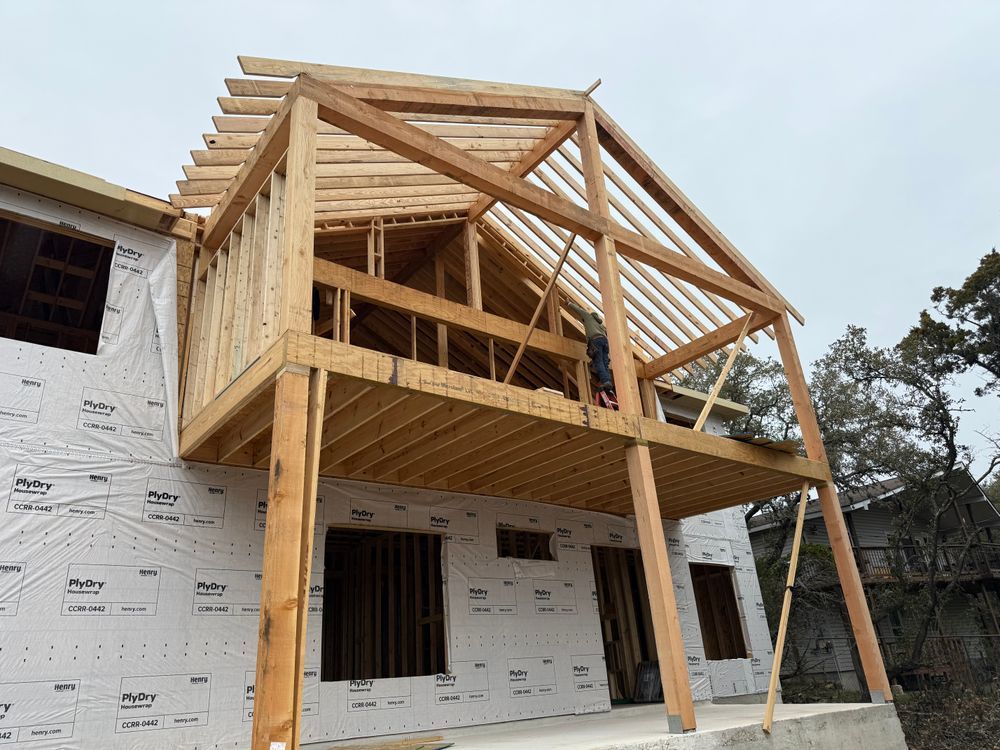 Wood-framed two-story house under construction with wraparound porch and exposed beams