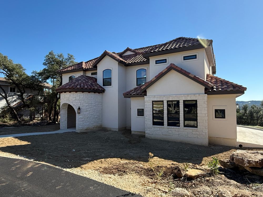 Two-story stucco house with red-tiled roof and arched entry on a sunny, unfinished lot