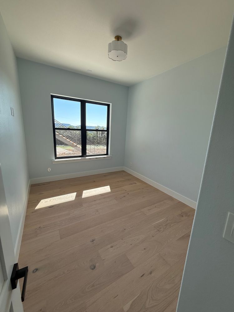 Empty light-blue bedroom with a window, wood floors, and sunlight on the floor.