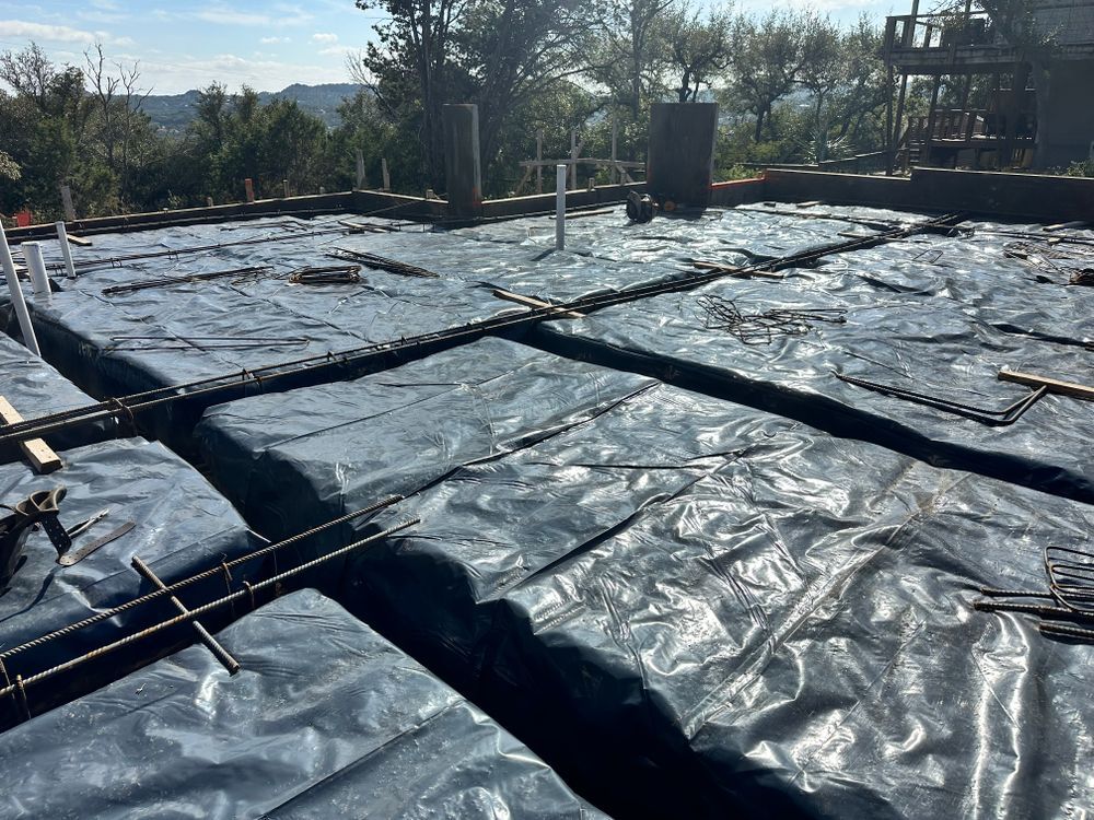 Black plastic sheeting covering a rooftop, with pipes and trees in the background