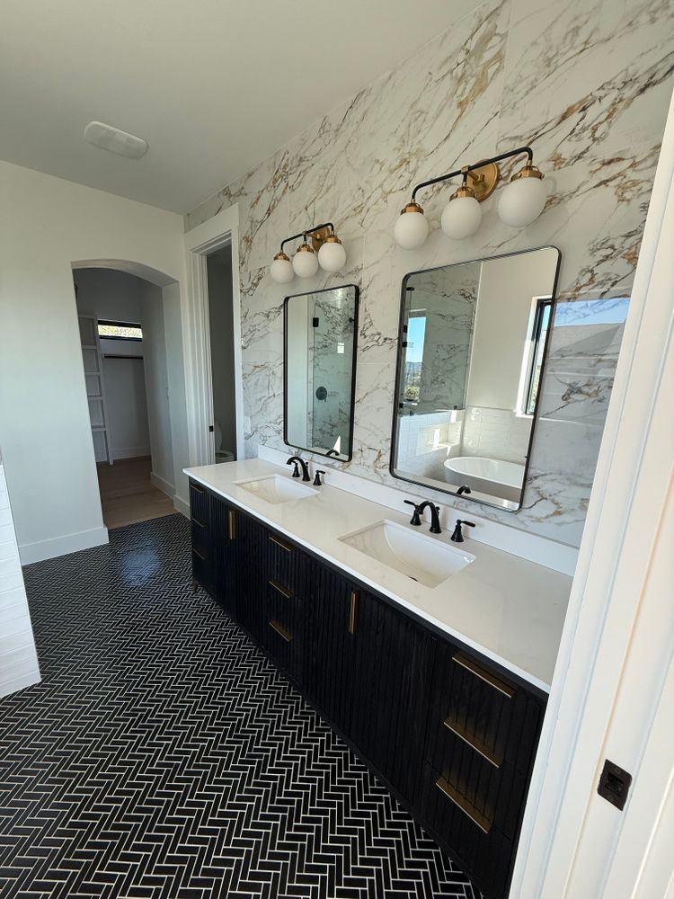 Modern bathroom vanity with double mirrors, white countertop, black cabinets, and herringbone floor.