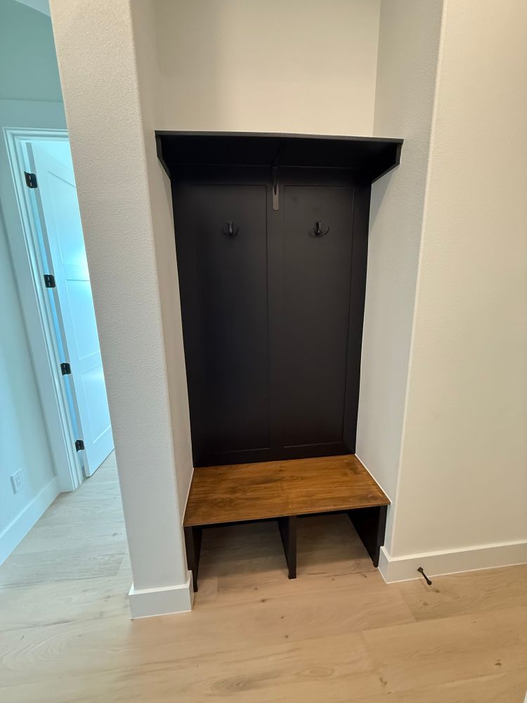 Black wall-mounted storage nook with shelves and a wooden bench in a hallway