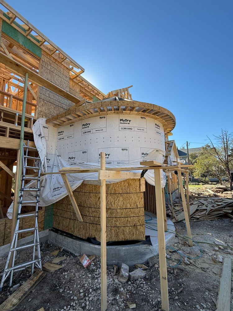 Partially built round house under construction with scaffolding and exposed framing on a sunny site