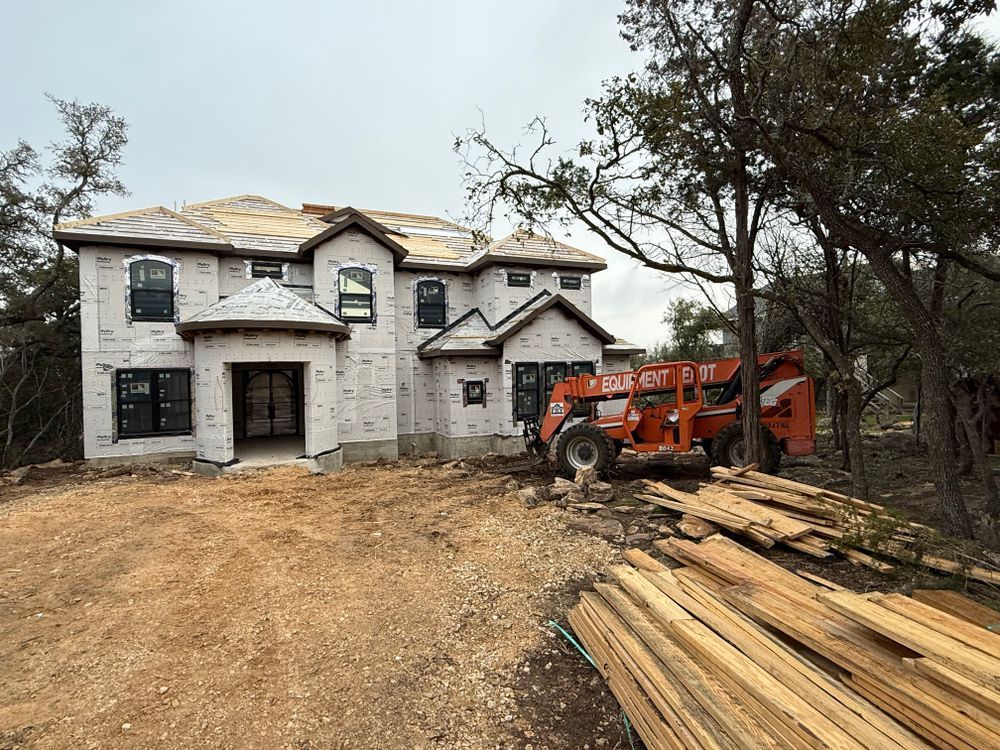 Two-story house under construction with an orange forklift and stacked lumber in the driveway