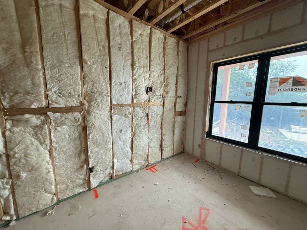 Unfinished room with insulated walls, exposed ceiling beams, and a large window letting in daylight.