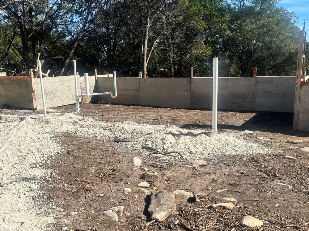 Partially built concrete foundation with walls and white support posts in a dusty outdoor lot