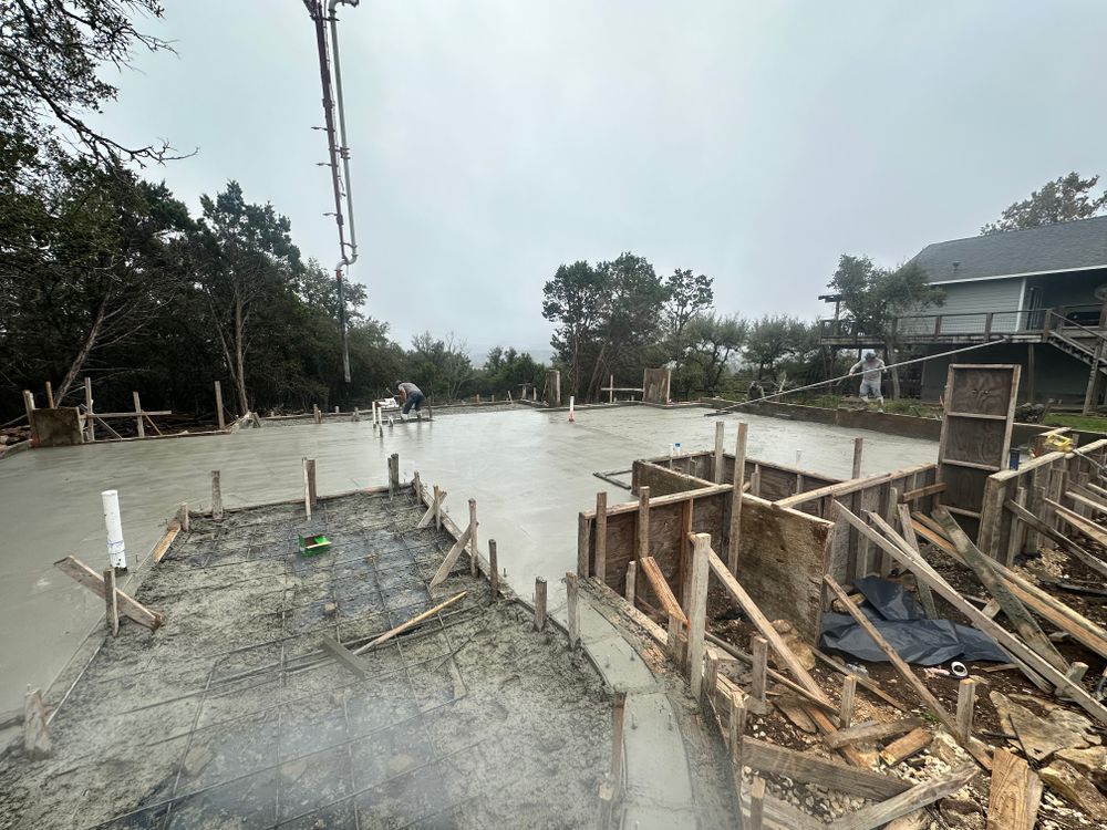 Damaged concrete roadway under repair with rebar, wooden forms, and muddy debris beside houses