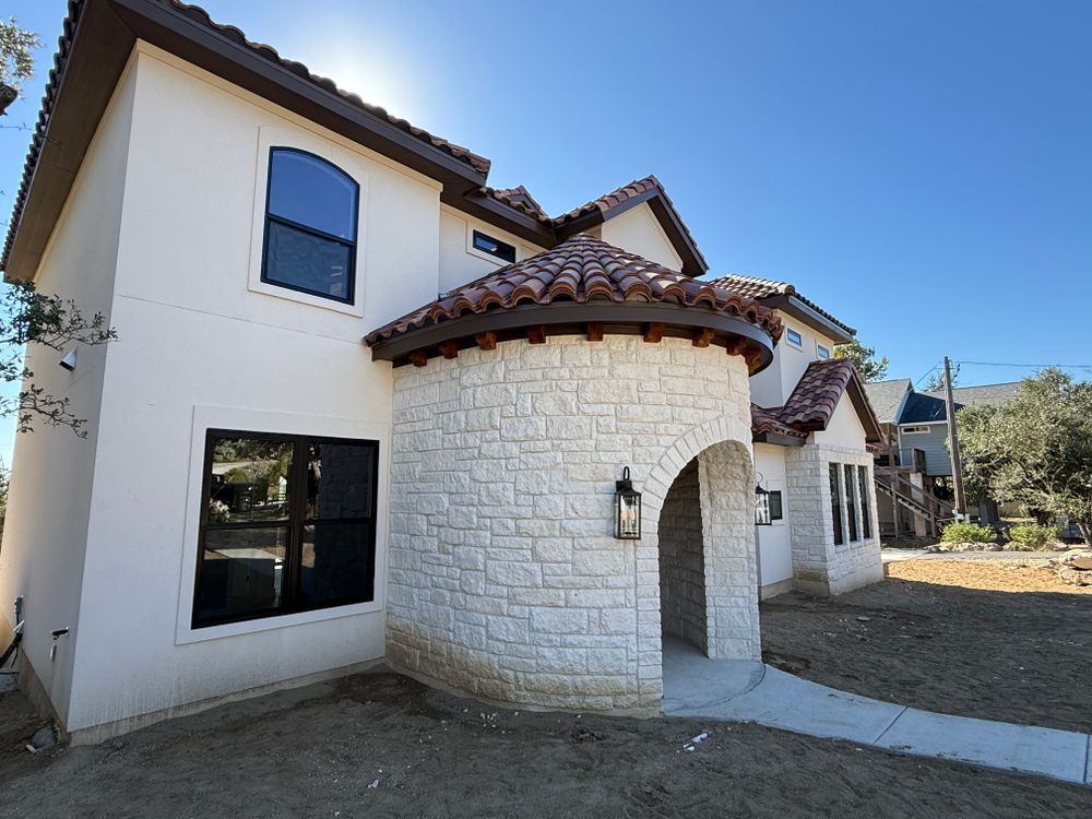 Stucco house exterior with arched entry, red tile roof, and large windows under a clear blue sky