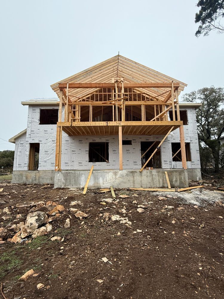 Two-story house under construction with exposed wooden framing and stone exterior walls