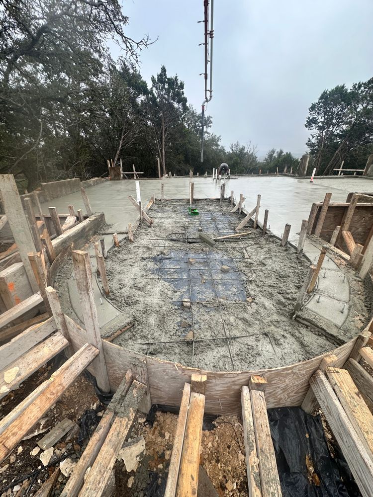 Concrete foundation under construction with wooden formwork, rebar, and a tall crane in the background.