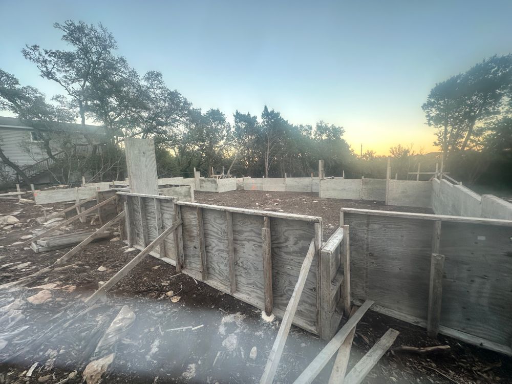 Concrete foundation forms at a construction site at sunset, with trees and a clear sky in the background