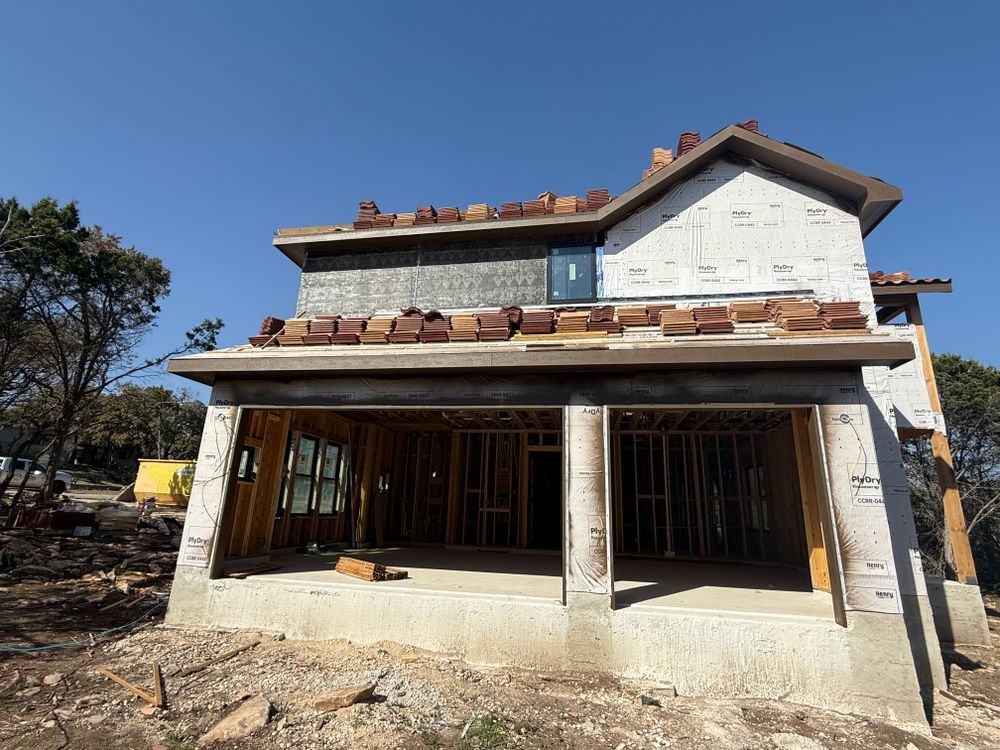 Partially finished two-story house with stone facade and covered porch under a clear blue sky