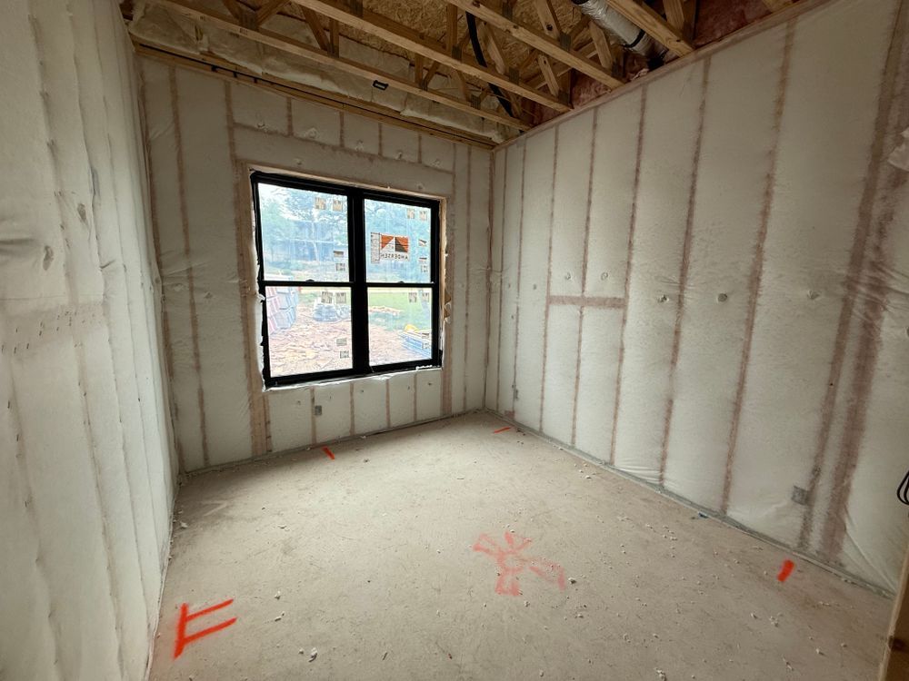 Unfinished room with insulated walls, exposed rafters, and a single black-framed window.