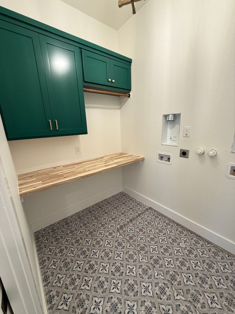 Small laundry room with green cabinets, butcher-block shelf, gray patterned floor, and washer hookups on the wall