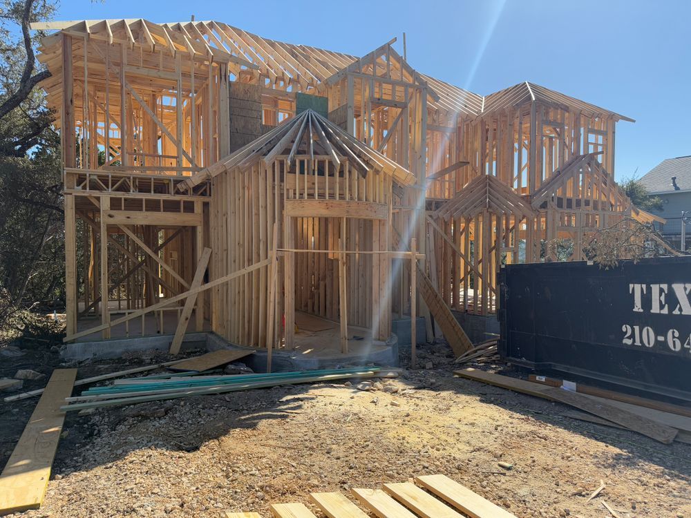 Partially framed two-story house under construction with a dumpster in front and dirt lot