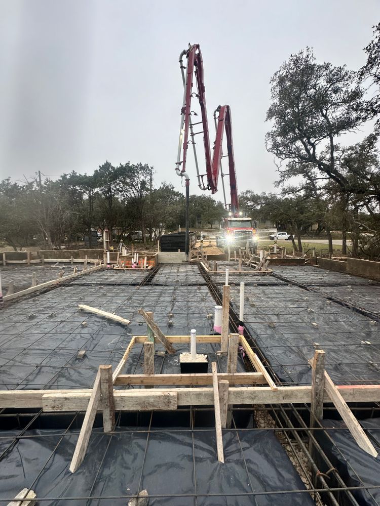 Concrete foundation site with rebar, wooden formwork, and a red crane in the background
