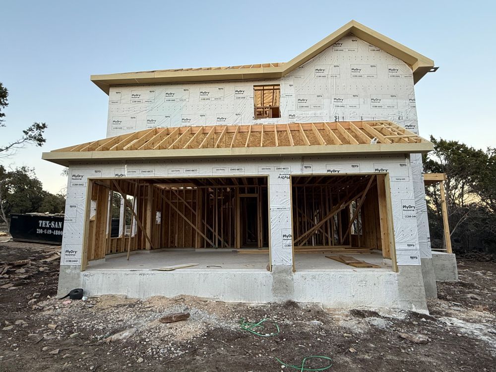 Partially built two-story house wrapped in white house wrap, with exposed framing and unfinished porch.