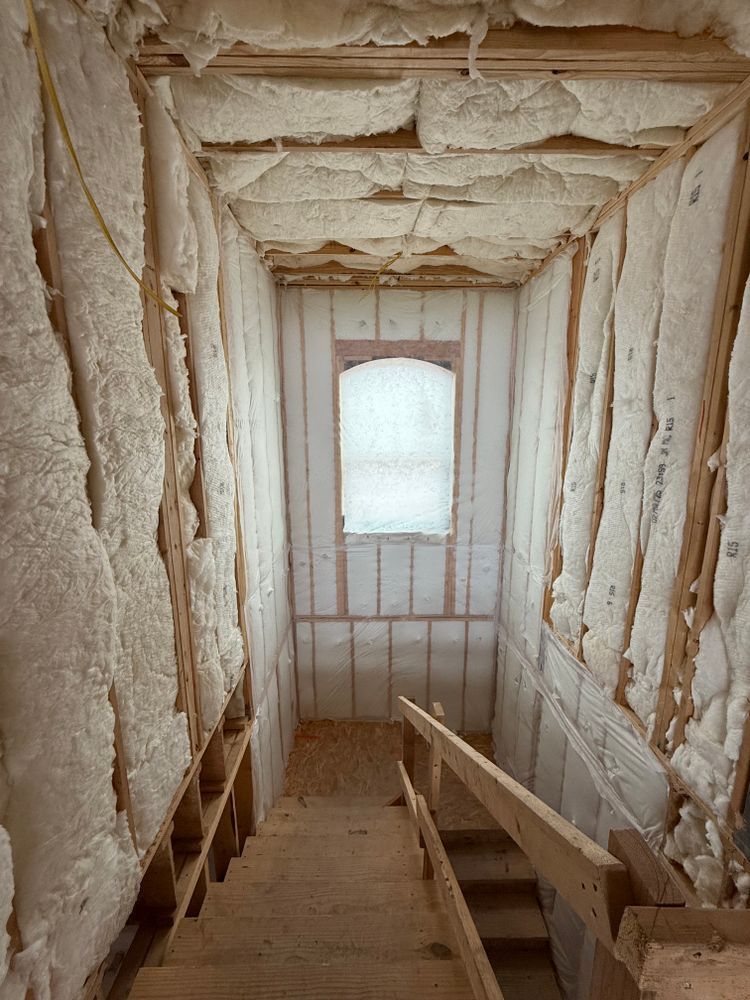 Insulated attic stairwell with unfinished walls and a window at the far end