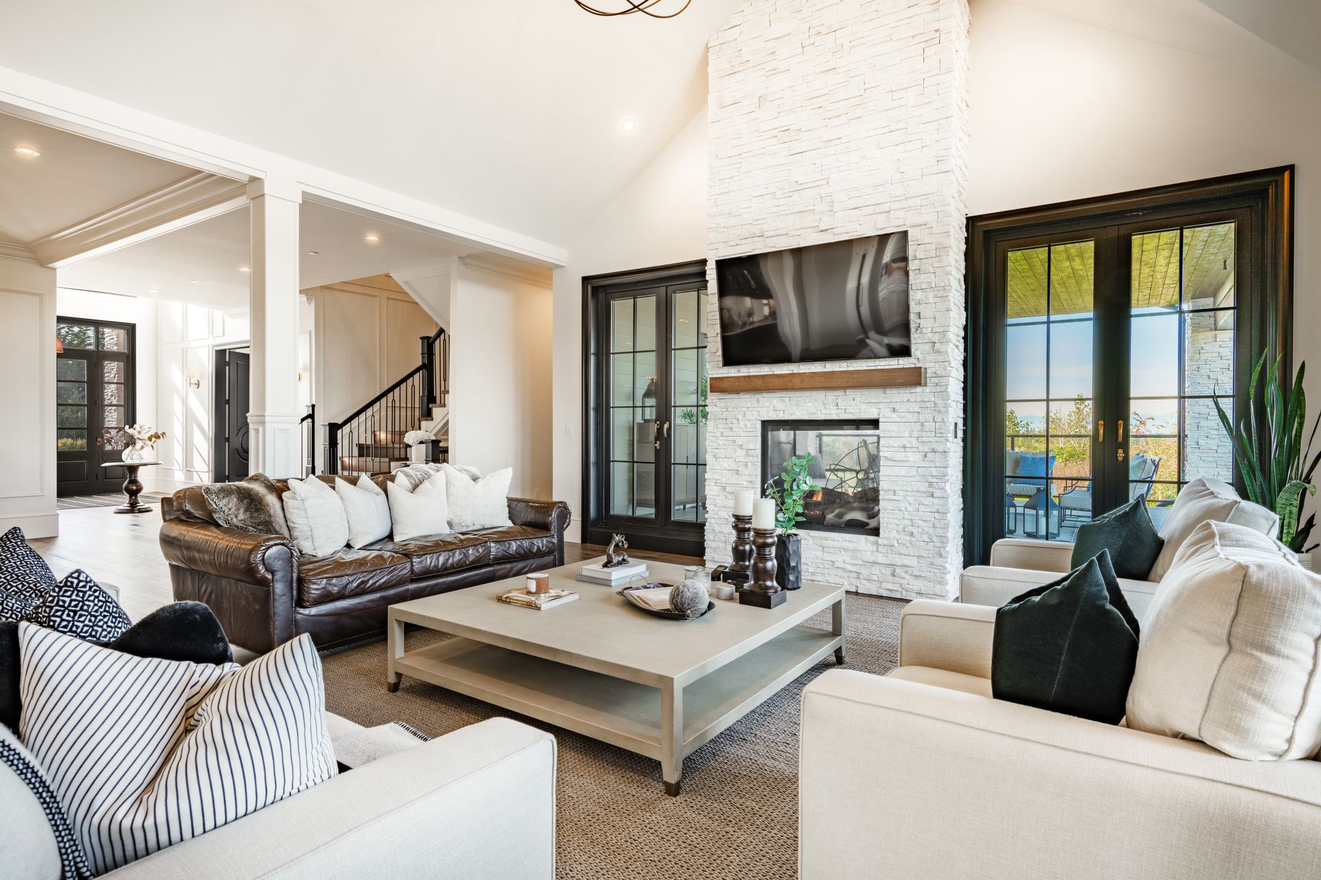 Bright, modern living room with white sofas, stone fireplace, dark windows, and a large coffee table