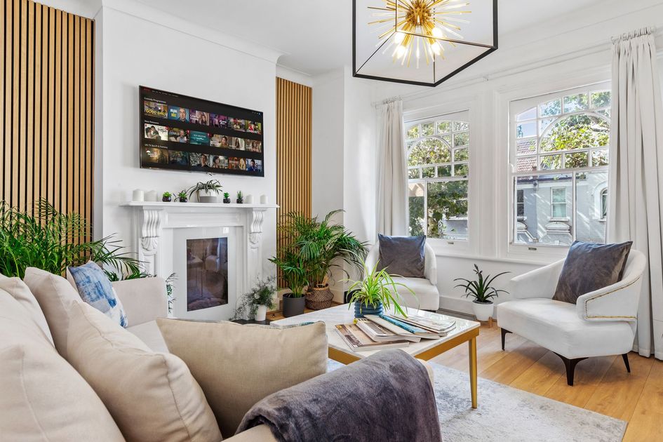 Bright living room with beige sofas, white fireplace, large windows, plants, and a modern chandelier