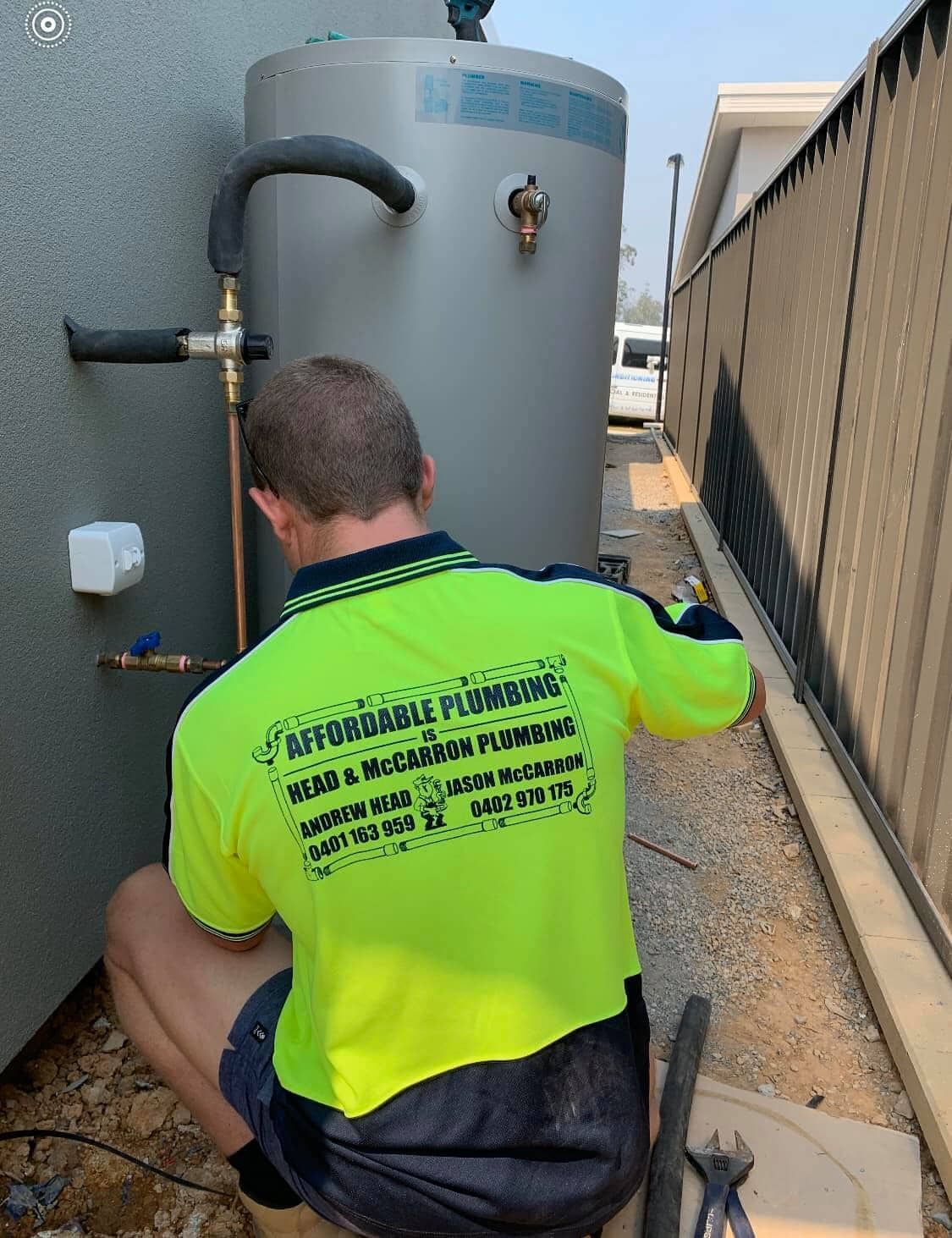 A Man in a Neon Yellow Shirt is Working on a Water Heater — Affordable Plumbing In Port Macquarie, NSW