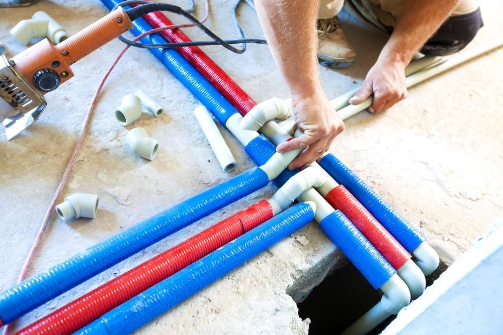 A Man is Installing Water Pipes in a Hole in the Floor — Affordable Plumbing In Laurieton, NSW