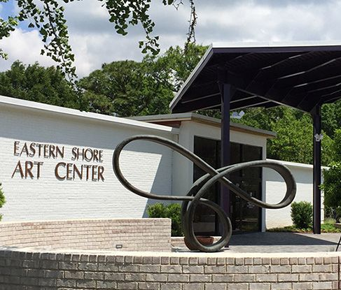 The white brick Eastern Shore Art Center building exterior with a modern, twisted metal sculpture in the foreground.