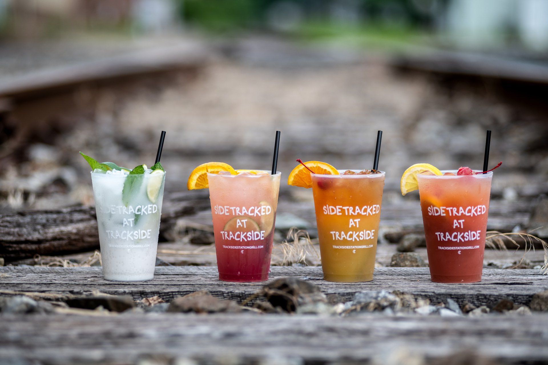 Three drinks are sitting on a wooden table next to train tracks.