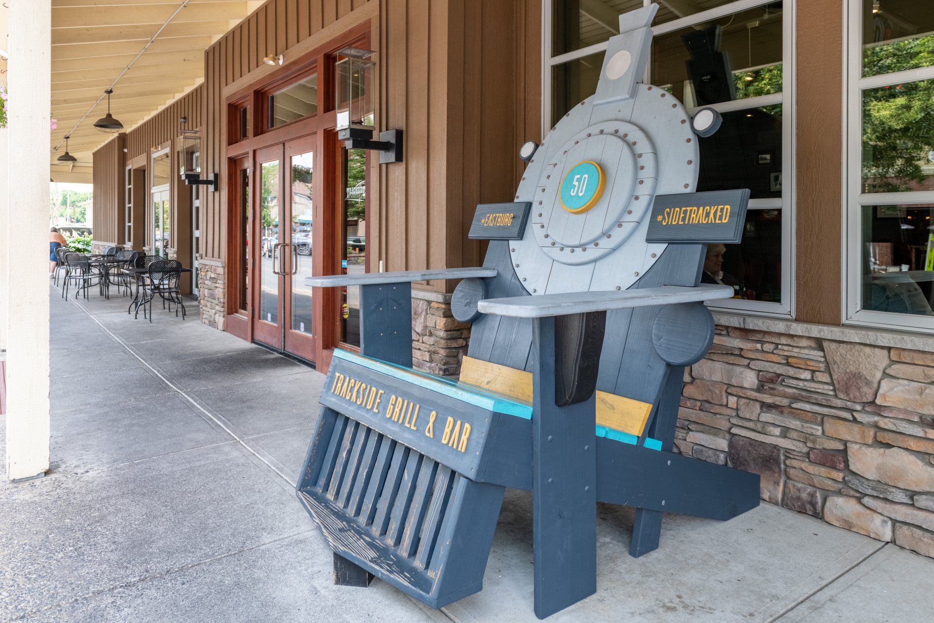 A large wooden chair in the shape of a train engine is sitting outside of a building.