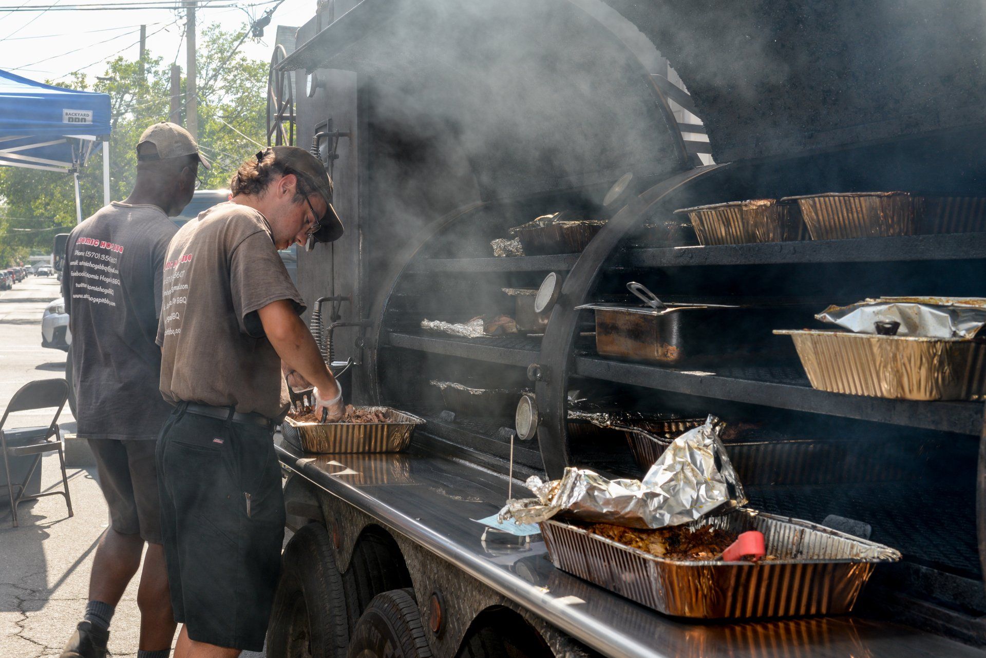 Two men are standing in front of a food truck cooking food.