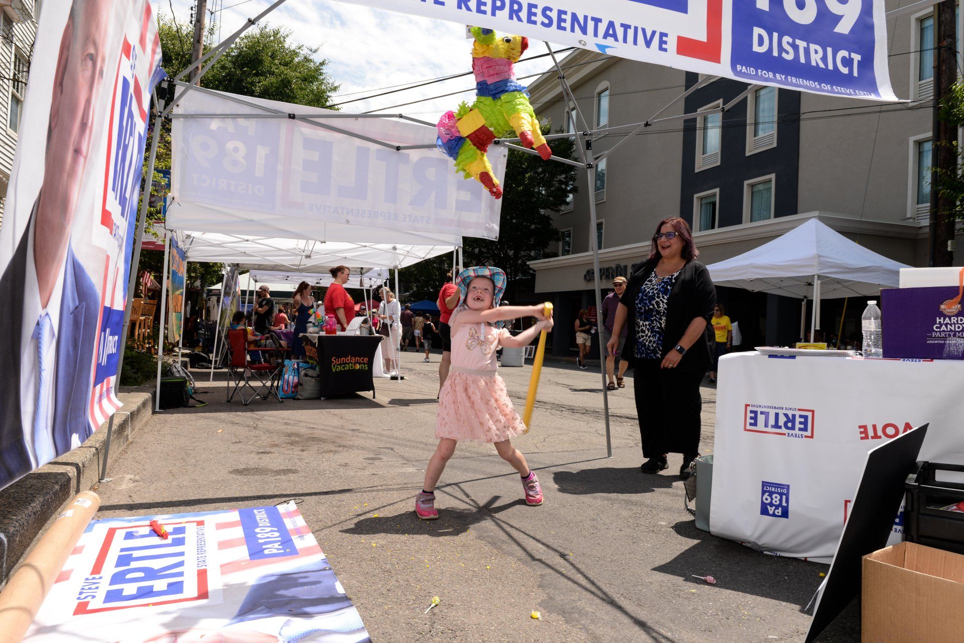 A little girl is throwing a piñata in front of a sign that says representative district