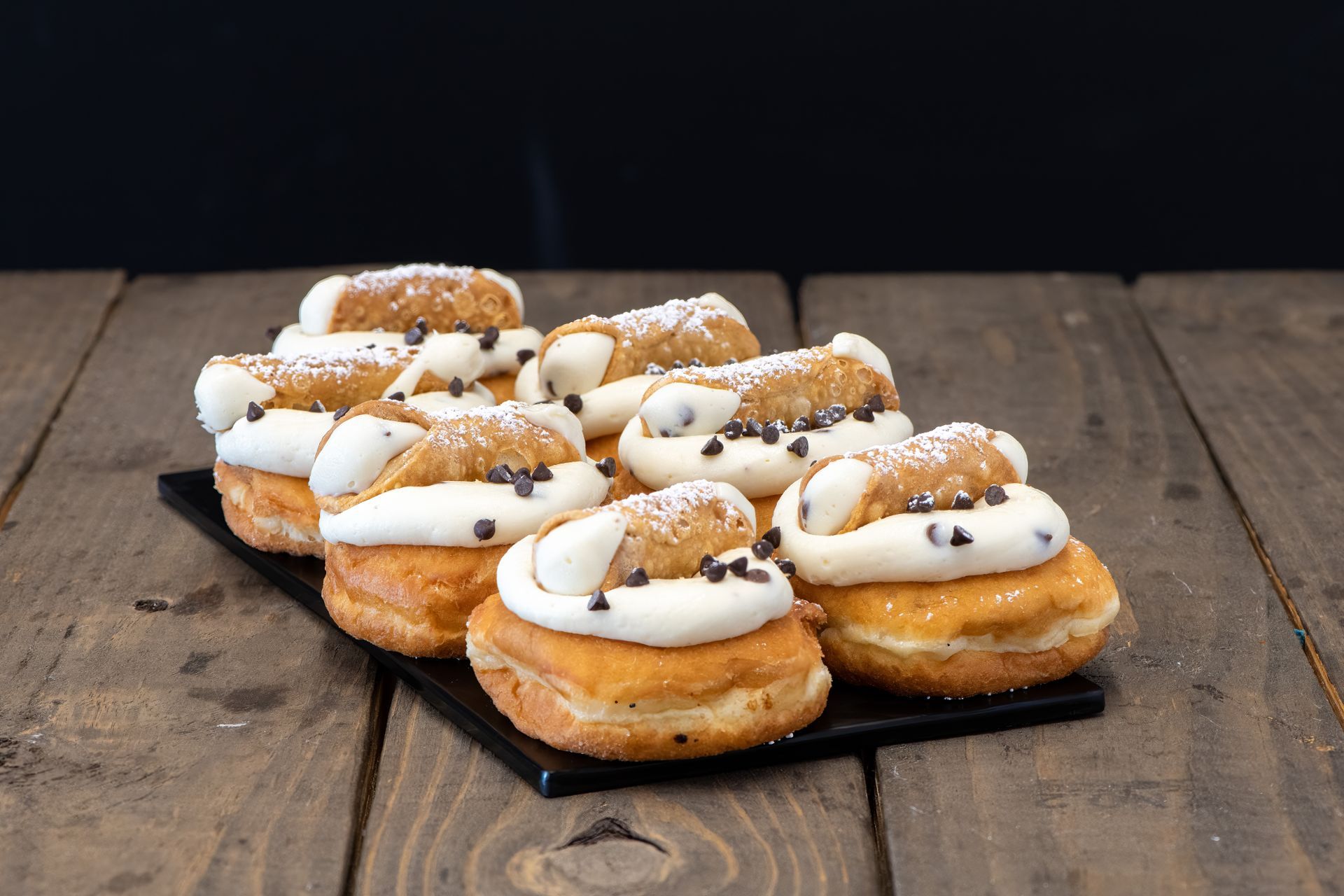 A tray of donuts with whipped cream and chocolate chips on a wooden table.